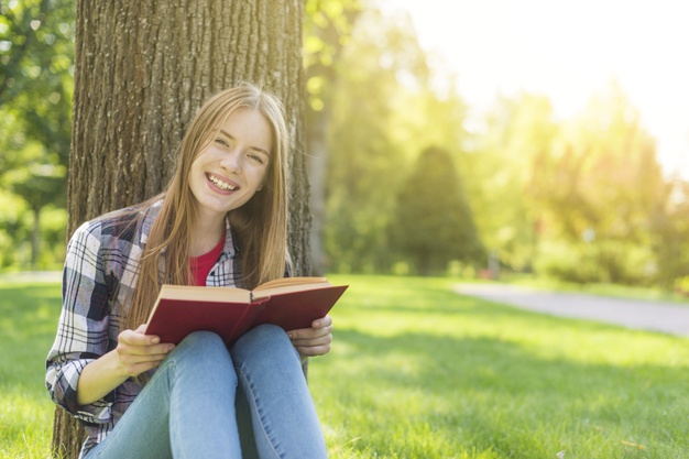 front view happy girl reading book while sitting grass 23 2148260057