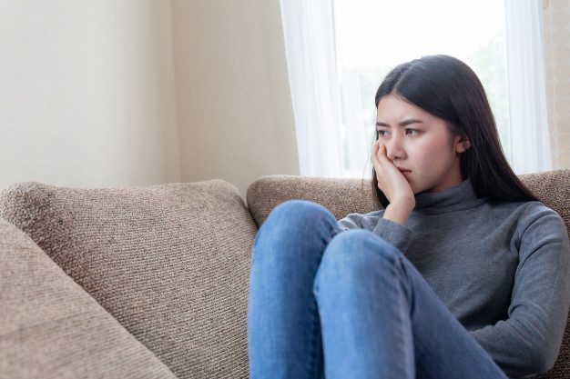 close up face unhappy asian pretty young woman sitting alone couch 1150 15513