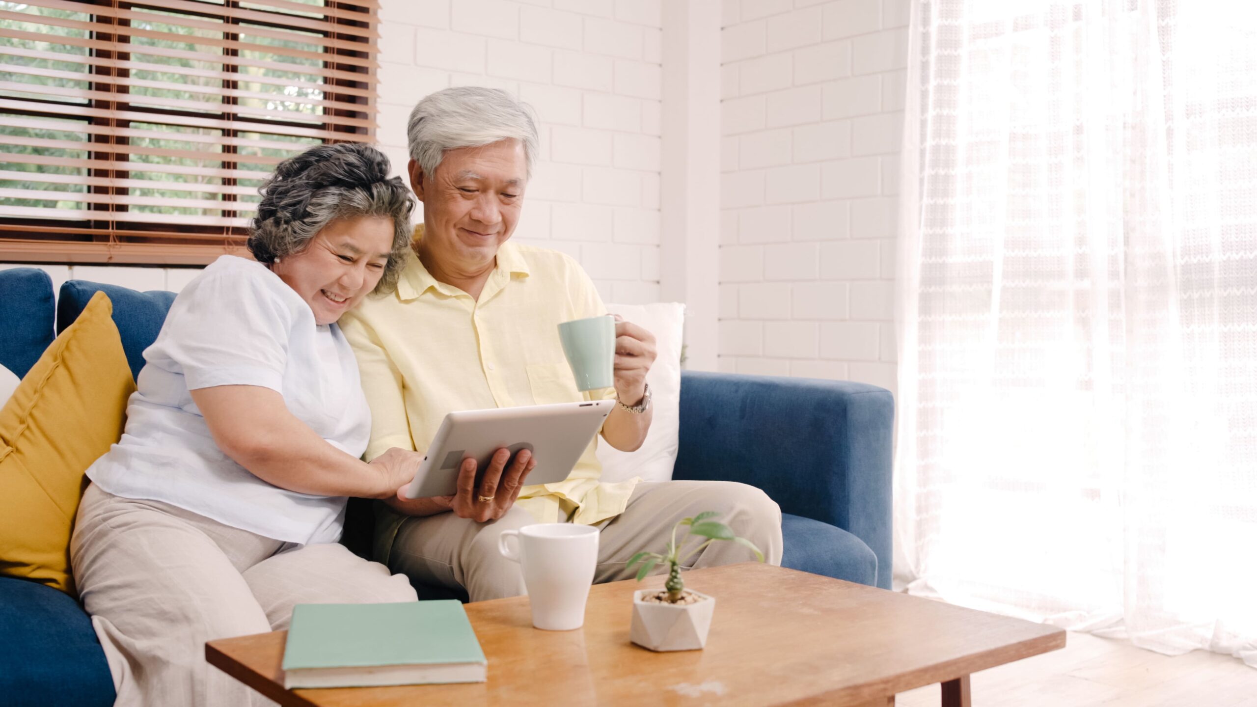 asian elderly couple using tablet drinking coffee living room home couple enjoy love moment while lying sofa when relaxed home 2 scaled