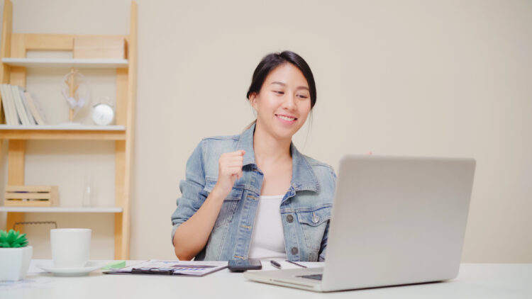 Young asian woman working using laptop on desk in living room at home. Asia business woman success celebration feeling happy dancing at home office. Enjoying time at home concept.