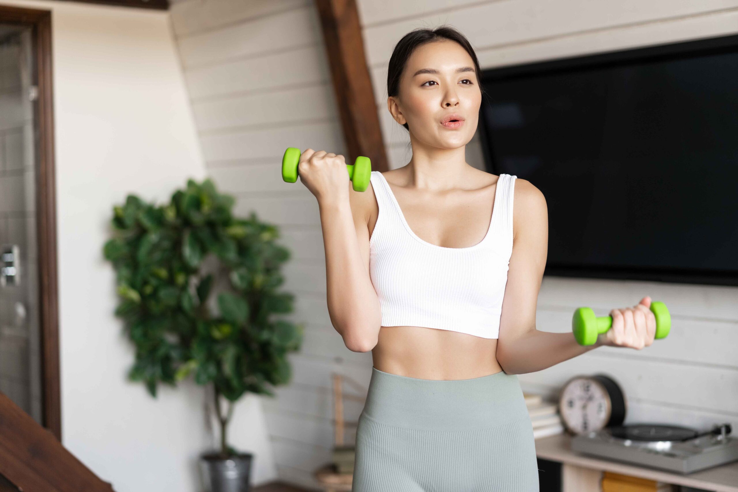 fitness asian girl doing workout home living room lifting dumbbells wearing activewear spo 11zon scaled