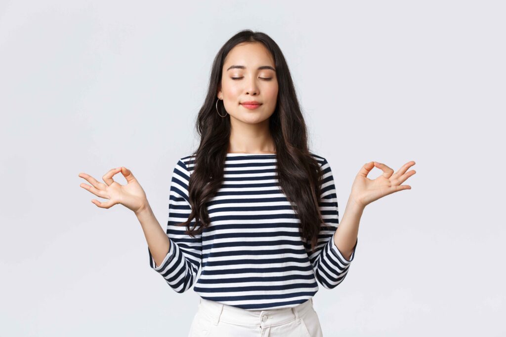 lifestyle people emotions casual concept relaxed patient smiling young asian woman with closed eyes meditating calm down breathing exercises with hands zen gesture 11zon